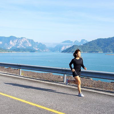 Asian woman running on road with mountain and lake background