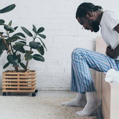 young african american man suffering from stomach ache while sitting on bed