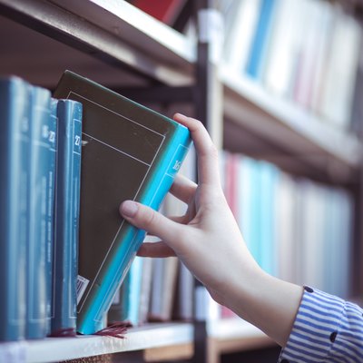 Hand of woman selecting a book from book shelf