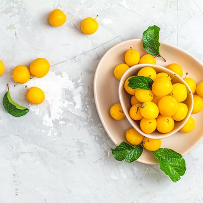 Creative summer pattern made of fresh yellow cherry plums in pink bowl on gray concrete background.