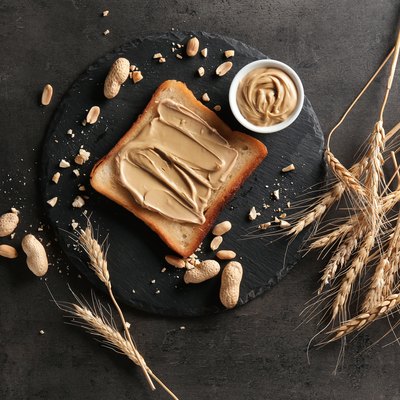 Slate plate with tasty toast and peanut butter on table