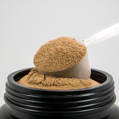 A cup of whey protein powder for muscle gains or diet person is in a plastic bottle on white background