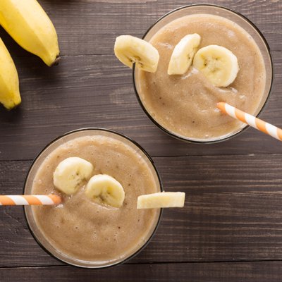 Banana smoothie and fresh banana on wooden background