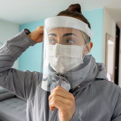 Woman at home wearing a facemask and adjusting her face shield to avoid COVID-19