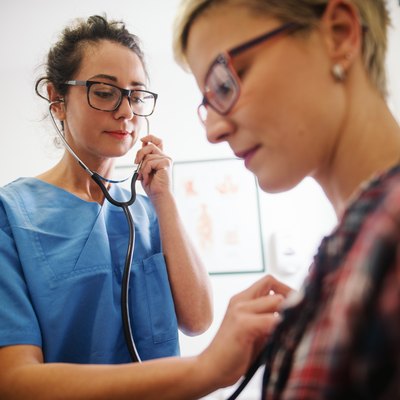 Female middle-aged doctor using stethoscope to examine patient.