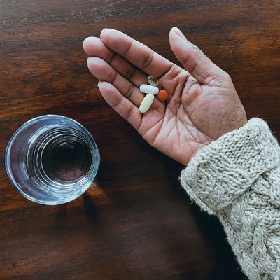 Woman Holds Daily Dose of Pills Next to Glass of Water