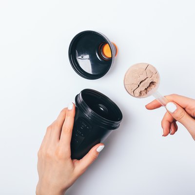 Woman's hands putting scoop of chocolate protein