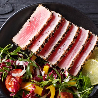 Top view of seared tuna steak, sliced and served with lime and a fresh salad