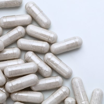 Pile of capsules with probiotic powder inside on white background.