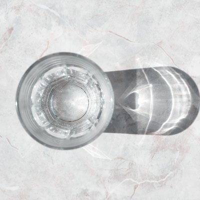 Glass of clear water on a white granite table in daylight, top view