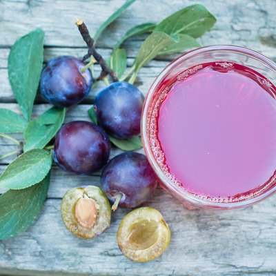 Plum juice in glass on wooden table background. Natural Green Leaf Background. Copy space
