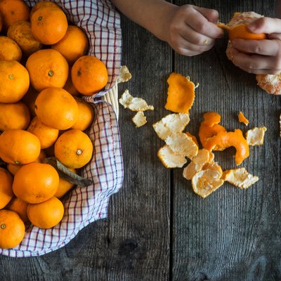 Cropped Hands Peeling Oranges On Wooden Table