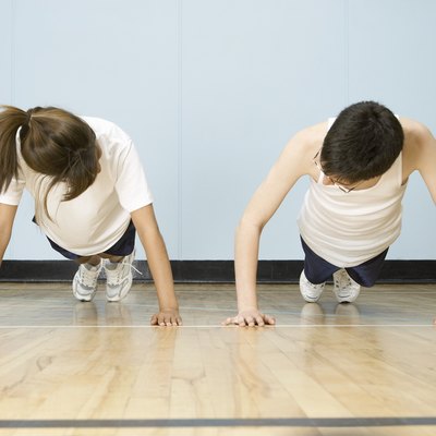 Teenage boy and girl (12-14) doing push-ups side by side in gymnasium