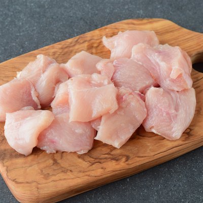 Raw chicken fillet cut in big cubes on a olive wood cutting board on a grey abstract background. Step by step cooking