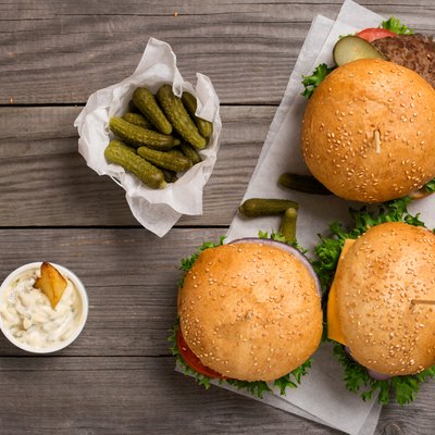 different hamburger on wooden table with sauces, fries and pickl