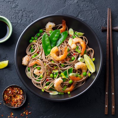 Stir fry noodles with vegetables and shrimps in black bowl. Slate background. Top view.