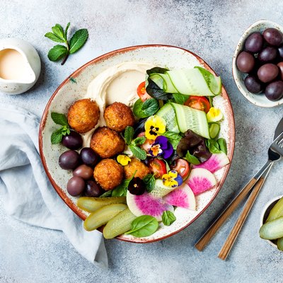 Middle eastern lunch Buddha bowl with hummus, falafel, tomato and greens salad, olives, pickles and edible flowers