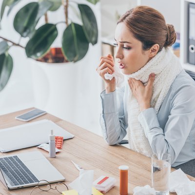 adult ill businesswoman with cough sitting at workplace in scarf