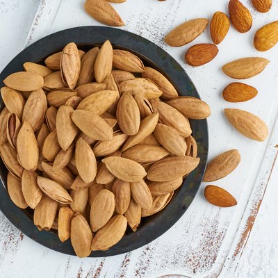 Top view plate with almonds in endocarp, bowl with drupe in shell on a white wooden cutting board. White background, overhead, copy space.