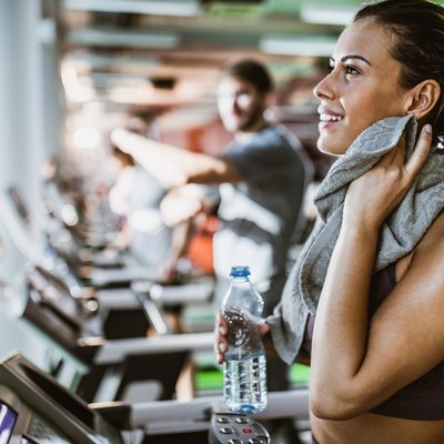 Happy athletic woman cleaning sweat during water break on a treadmill in a gym.