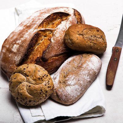 Tasty dark bread and buns on white background, copy space. Bakery products, wholemeal bread and brown whole wheat buns