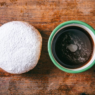 Coffee and krapfen with powder sugar, two, top view and isolated, wooden background.