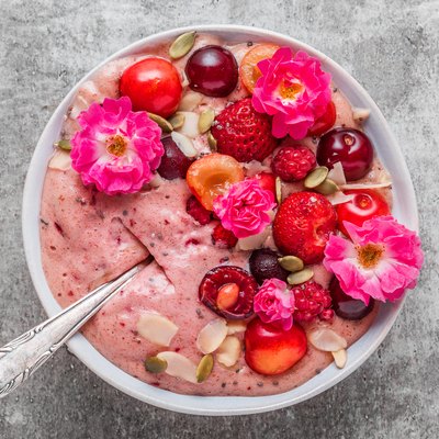 bowl of pink berry smoothie or nice cream made of frozen fruits and nuts with fresh berries, nuts and rose flowers