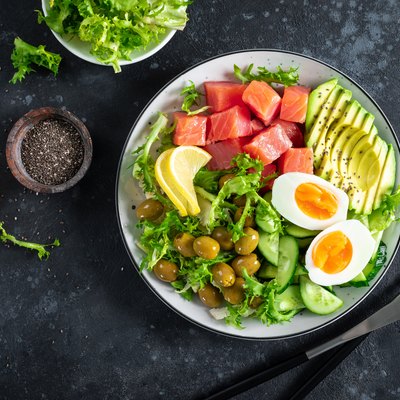 Ketogenic, paleo diet lunch bowl with salted salmon fish, lemon, avocado, olives, boiled egg, cucumber, green lettuce salad and chia seeds, healthy food trend, top view