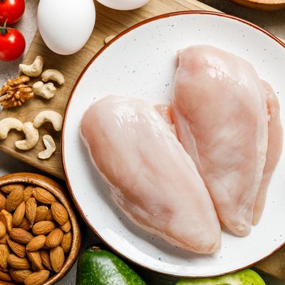 top view of fresh raw chicken breasts near nuts, eggs and vegetables, ketogenic diet menu