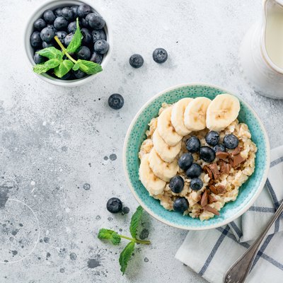 Oat porridge with banana, chocolate and fresh blueberry in a bowl on a light gray slate, stone or concrete background. Top view.