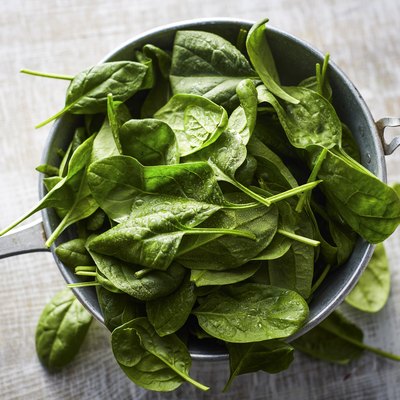 Fresh spinach leaves in colander on wood
