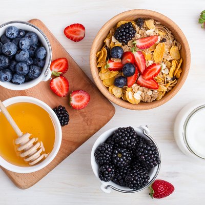 Healthy breakfast with cereal, fresh berries, yogurt and honey over white rustic wooden table viewed from above