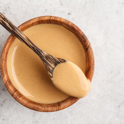 Creamy homemade peanut butter in wooden bowl, top view.