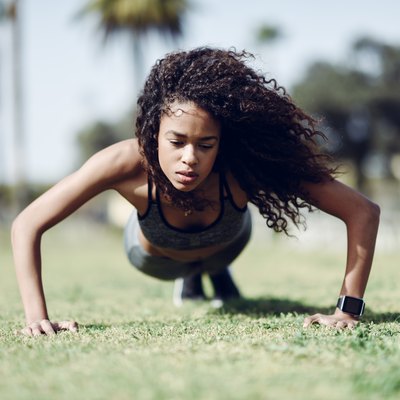 Sporty young woman doing push-ups on lawn