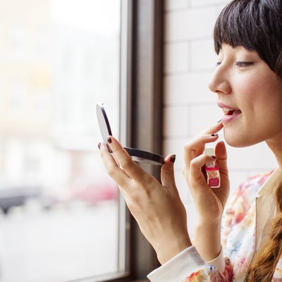 Woman applying lipstick while sitting in bar