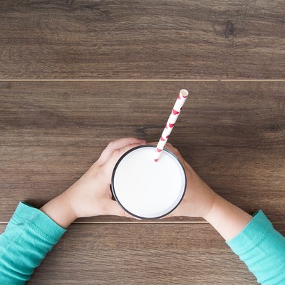 Child holding a glass of milk on dark rustic table