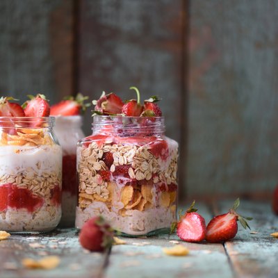 Tasty healthy breakfast. Overnight raw oatmeal in jars with organic strawberries on turquoise background
