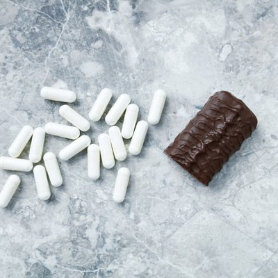 High Protein bar and Arginine capsules. Bodybuilding food supplements on bright stone background. Directly Above. Copy space.