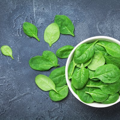 Green spinach leaves in bowl on black table top view. Organic and diet food.