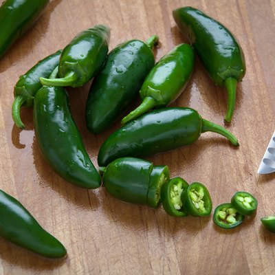 Jalapeños whole and chopped with knife on wood cutting board.