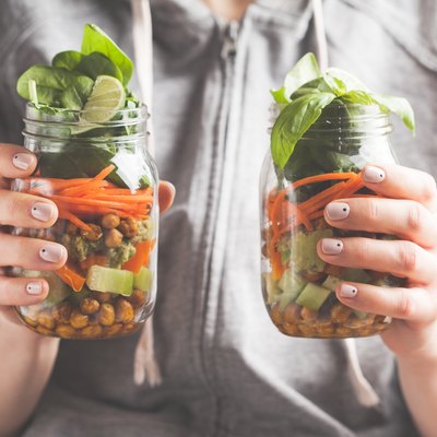 A woman holds and eats a salad in a glass jar with baked chickpeas, guacamole and vegetables. Healthy diet detox vegan food concept.