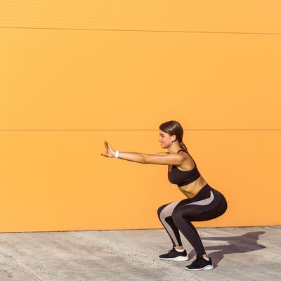 Young attractive woman practicing fitness, doing bodyweight squat exercise, yoga chair pose, working out, wearing black sportswear black pants and top,
