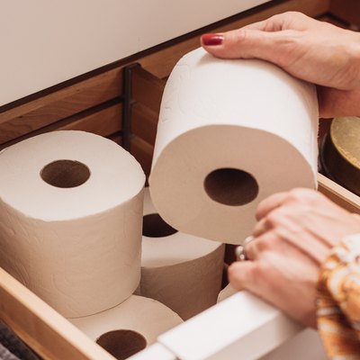 A woman reaching for a roll of toilet paper stored in a bathroom drawer