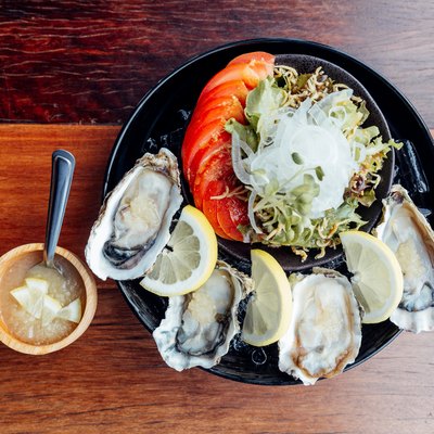 Fresh Oysters close-up on black plate, served table with oysters, lemon, ice and salad.