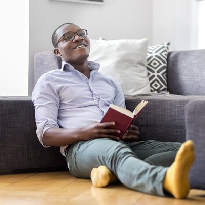 Happy young man sitting on the floor in the living room reading book