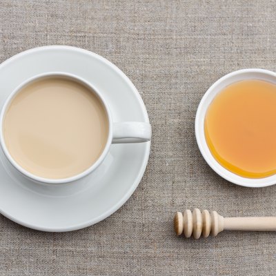 Spicy warming tea with milk in a white porcelain cup with honey and honey dipper