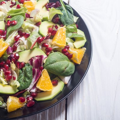 Leafy green salad with avocado, oranges and pomegranates on wooden table