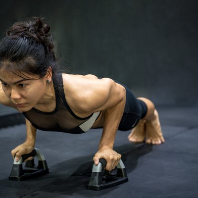 Young Asian athlete woman doing push up with push-up bars on the floor