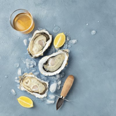 Fresh raw oysters, overhead shot on ice with a glass of white wine, lemon slices, shucking knife and a place for text