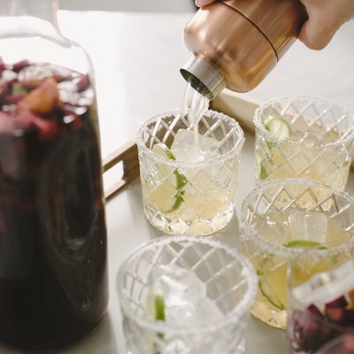 Cropped hand of man pouring drinks in glasses on table at home
